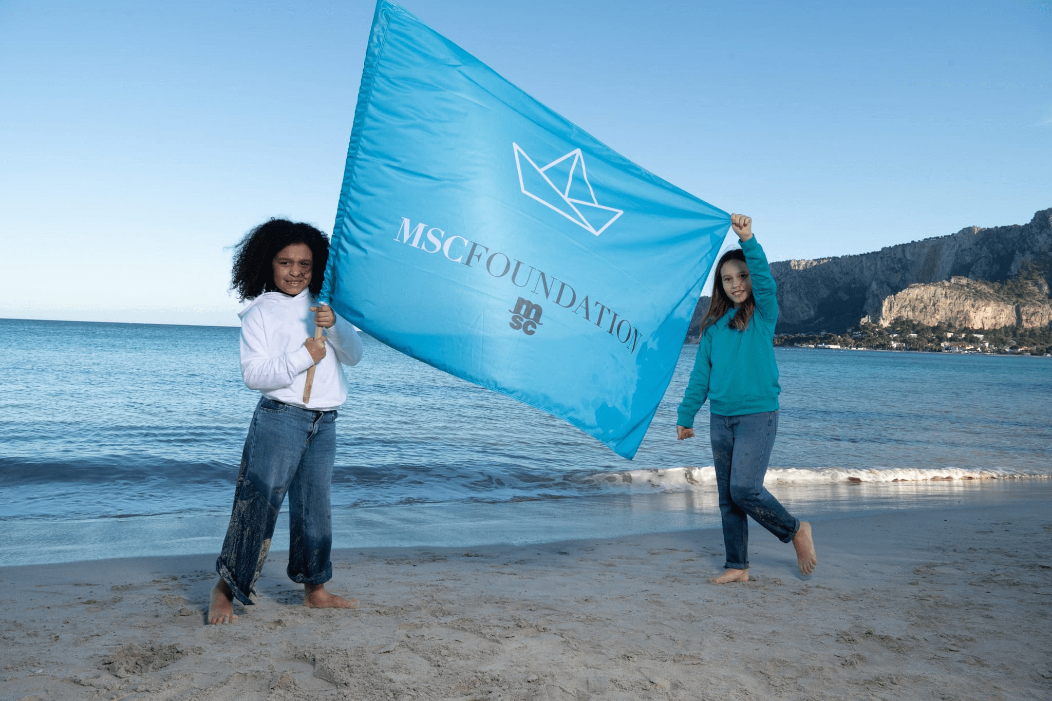 Children holding MSC Foundation flag on the beach
