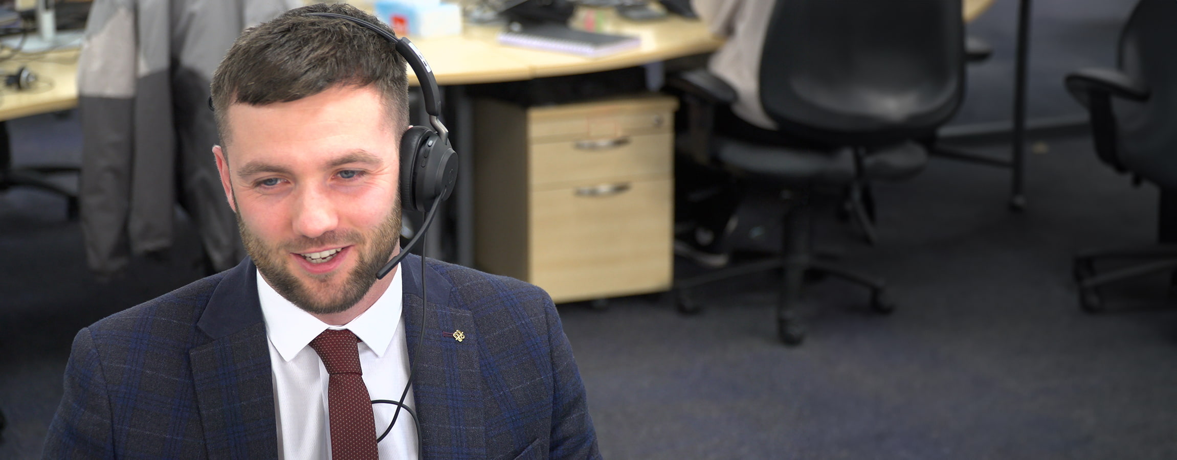 A smiling man wearing a headset and a suit is seen working at the MSC UK office, with the text 'Connecting UK Businesses to Global Markets' overlaid on the image. The background includes office furniture, such as desks and chairs, slightly blurred