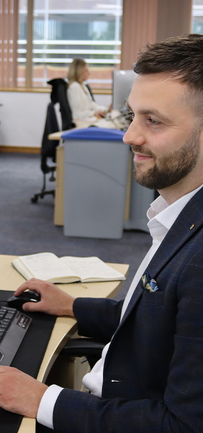 A smiling man wearing a headset and a suit is seen working at the MSC UK office, with the text 'Connecting UK Businesses to Global Markets' overlaid on the image. The background includes office furniture, such as desks and chairs, slightly blurred