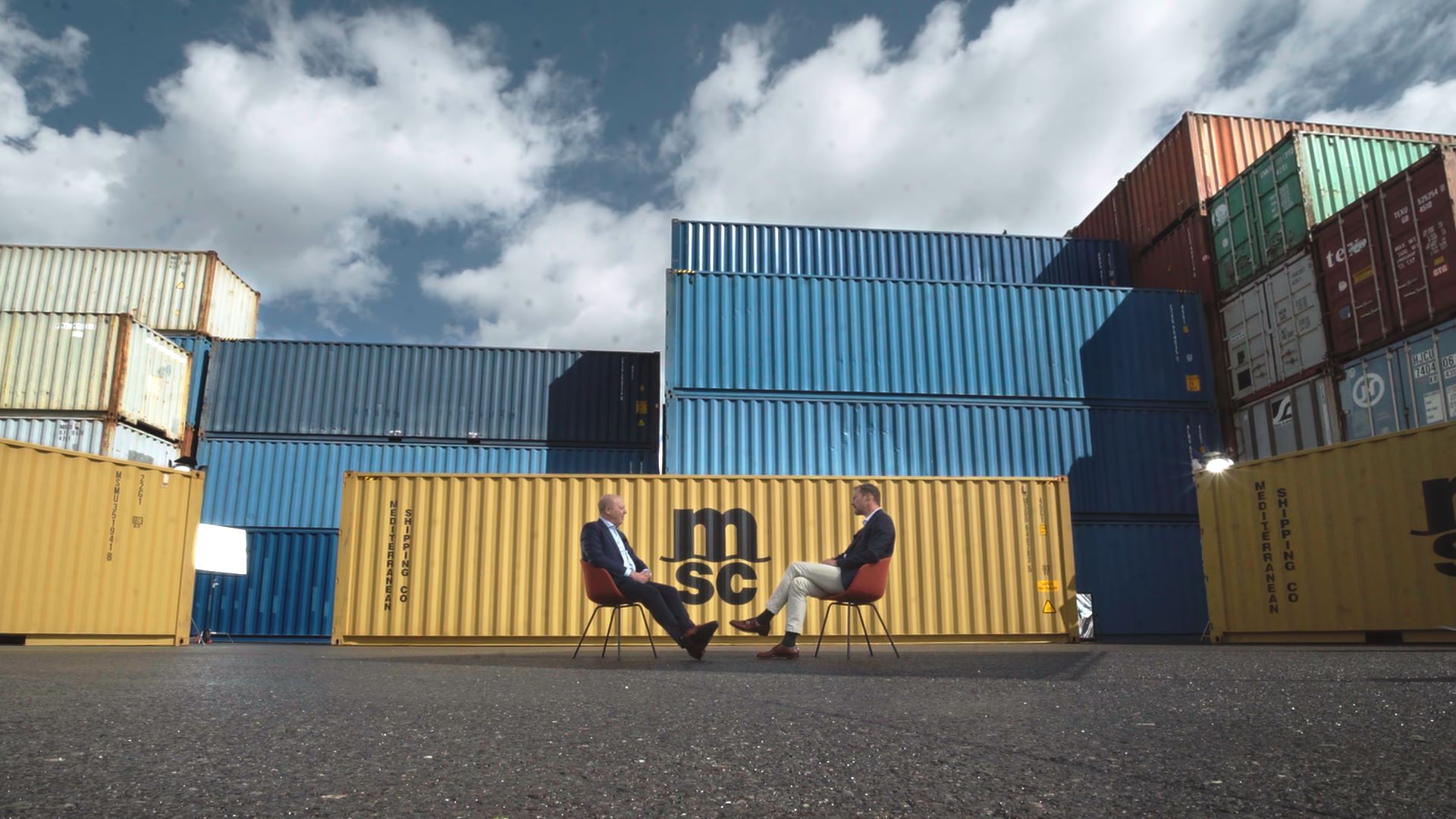 Andre Simha and Thomas Bagge sitting across each other talking with containers stacked in the background
